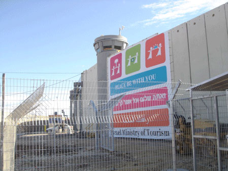 photo: large sign hangs on tall concrete wall with guard tower